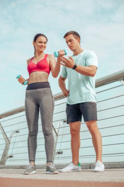 Genç adam ve kadın halterleri açık havada eğitimdeler.