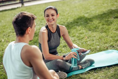Parkta paspasın üzerinde oturmuş bir adamla konuşan gülümseyen bir kadın.