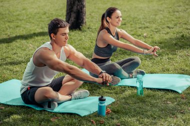 Erkek ve kadın parkta paspaslar üzerinde birlikte egzersiz yapıyorlar.