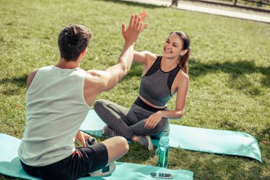 Kadın ve erkek sporcular parkta egzersiz yaptıktan sonra beşlik çakıyorlar.