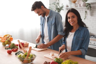 Kadının kameraya gülümsemesiyle sebze kesen koca portresi.