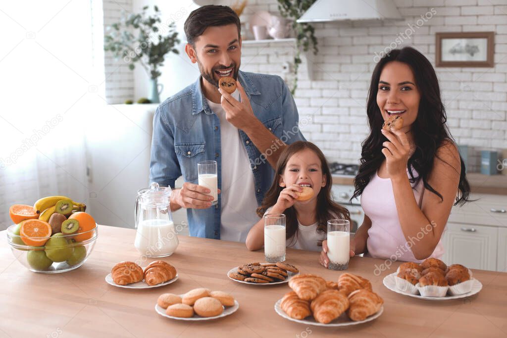 portrait of happy family eating cookies with milk and looking at the camera