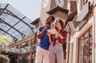 Genç bir kadın ve bir adam güneşli bir günde dışarıda dijital tabletteki adama bakıyor.