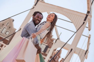 Afrika kökenli Amerikalı bir adam, Asyalı bir kadını elinde tutuyor ve elinde alışveriş torbaları var.