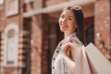 Çekici Asyalı kadın dışarıda alışveriş torbalarıyla kameraya bakıyor.