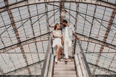 Alışveriş merkezinde yürüyen merdivende duran çiftin tam boy çekimi.