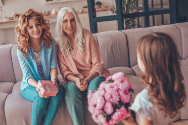 Anneler Günü için anne ve büyükanneyi evde bir buket çiçekle sunan torun manzarası.