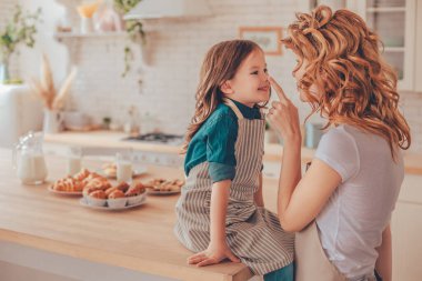 Anne, mutfak masasında otururken burnuna parmağıyla dokunuyor.