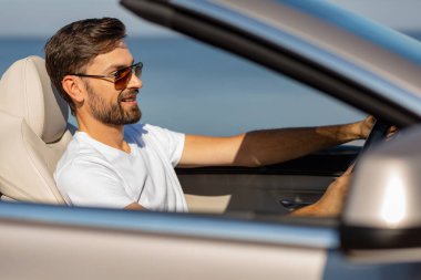 Güneşli bir günde üstü açık ata binen gülümseyen genç adamın yan görüntüsü