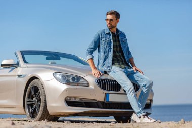 Yakışıklı adamın güneş gözlüğü takıp arabada oturduğu uzun bir çekim.