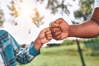 Yeşillik ve ağaçların arka planında arkadaşça yumruklaşan iki elin kesilmiş fotoğrafı.