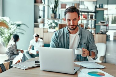 Kafede dizüstü bilgisayar kullanan gülümseyen bir iş adamı. Kahvehanede çalışırken kahve içen neşeli bir adam.