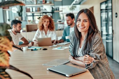 İş adamları arka plan üzerinde çalışırken neşeli iş kadını ofiste ayakta duruyor. Mutlu yüz ifadesi olan pozitif kadın.