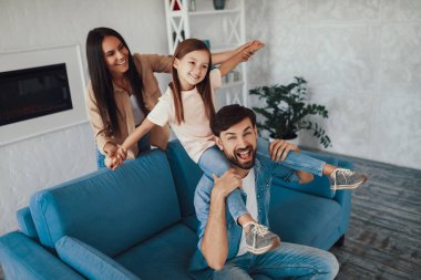 Güzel annesi ve komik babasıyla güzel bir kanepede eğlenirken mutlu çocuk gülümsüyor.