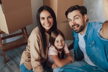 Genç esmer adam, çekici kadını ve güzel çocuğuyla kordonun yanında otururken selfie çekiyor.