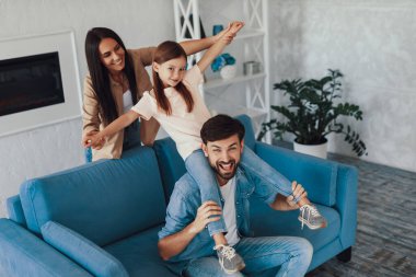 Kızını omuzlarına alıp karısıyla eğlenirken yüzünü buruşturan heyecanlı genç adam.