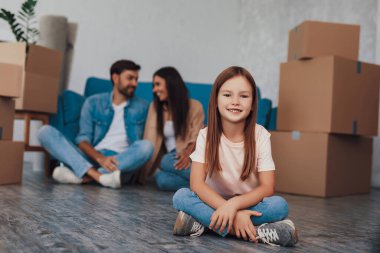 Annesi ve babası kanepenin yanında otururken, yerde çapraz çapraz oturan neşeli kızın seçici odak fotoğrafı.