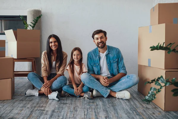 Üç heyecanlı aile yadigarı yerde bağdaş kurmuş, etrafı karton kutularla çevrili.