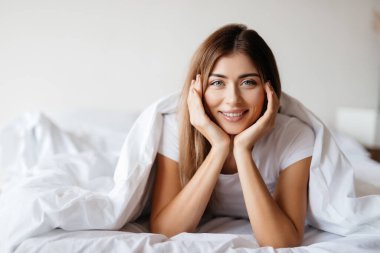 Rahat yatağından kameraya bakarken ellerini kaldıran sakin genç bir kadın.