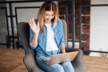 Arkadaşlarıyla video görüşmesi yaparken bilgisayarına el sallayan genç bir kadın.