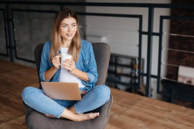 Takdire şayan genç bir kadının kucağında dizüstü bilgisayarıyla koltukta otururken çekilmiş fotokopi uzay fotoğrafı.