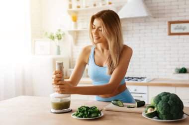 Mutfak blenderi kullanırken leziz meyve püresi yapmak için msiling yapan tatlı genç bir kadın.