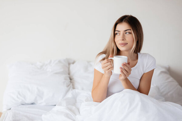 Copy-space photo of a calm fair-haired woman looking to the side while sitting in her bed and holding a coffee cup