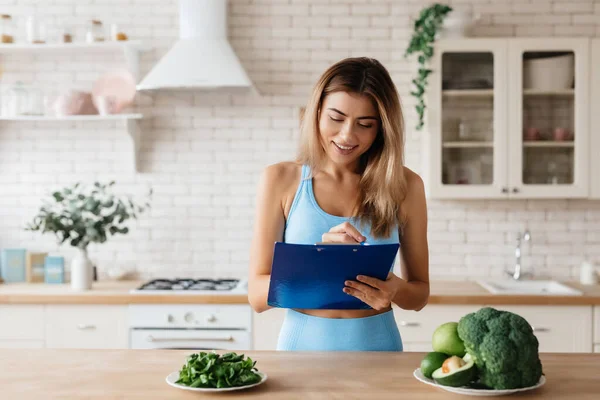 Atractiva Joven Mujer Sujetando Portapapeles Mientras Está Pie Cocina Mirando — Foto de Stock