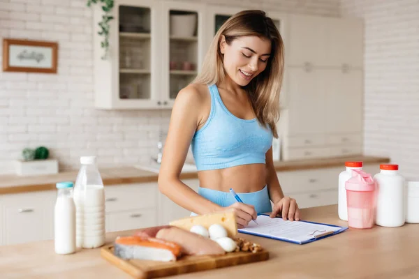 Attraktiv Dam Antecknar Och Står Nära Köksbordet Med Kött Mejeriprodukter — Stockfoto