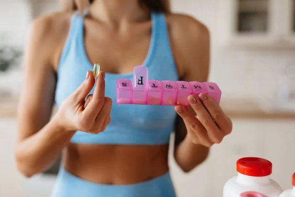照片上的年轻女子手上拿着一个装有维生素和透明药丸的粉色容器 — 图库照片