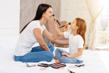 Mutlu kadın ve tatlı çocuğu yüz yüze oturup bacak bacak bacak üstüne atarken burun pudralıyorlar.