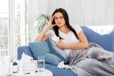 Endişeli, hastalıklı bir kadın gözlerini kapatıyor ve battaniyenin altında yatarken kaşlarını çatıyor.