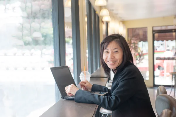 Business woman using computer sitting in a cafe with cocoa spin put on the right hand side. — Stock Photo, Image