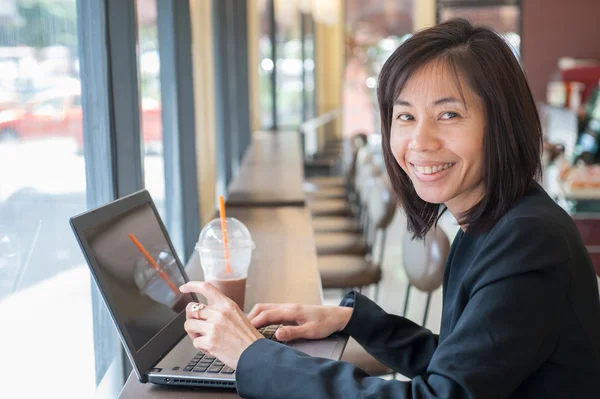 Business woman using computer sitting in a cafe with cocoa spin put on the right hand side. — Stock Photo, Image