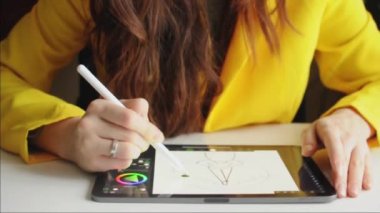 Kadın tablet üzerinde stil kullanarak resim çiziyor. Aydınlatıcı sarı giysiler içinde oturuyor..