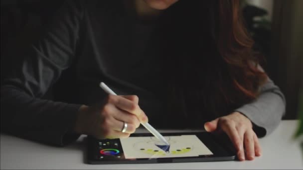 Жінка малює на тачпадку зі стилусом, що сидить у сірому одязі — стокове відео