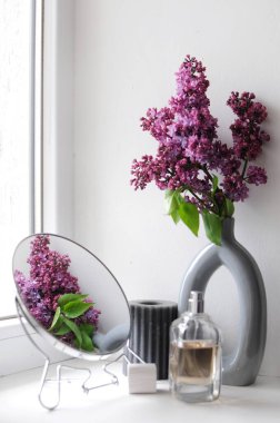 Beyaz arka planda leylak çiçekli parfüm şişesi. Aynalı kompozisyon