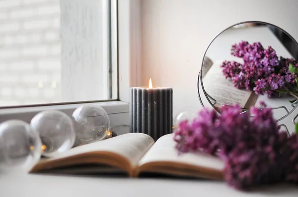 Romantic cozy corner at home with opened book, candle and with a lilac bush. — Stock Photo, Image