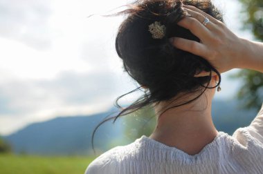 Bir kız elinde küçük bir çiçekle saçını tutuyor. Doğal saç stili