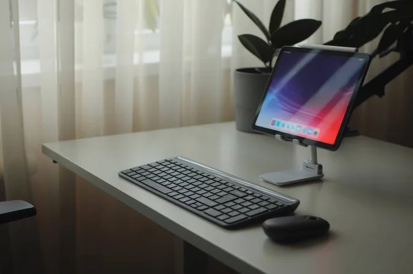Elegante local de trabalho doméstico com dispositivo tablet em stand com mouse e teclado — Fotografia de Stock