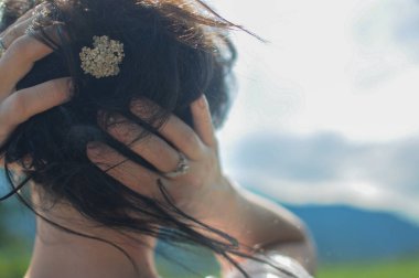 Bir kız elinde küçük bir çiçekle saçını tutuyor. Doğal saç stili