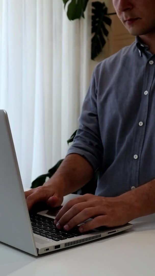 Vídeo vertical de un joven trabajando en el ordenador portátil.Trabajo desde el hogar minimalismo interior — Vídeos de Stock