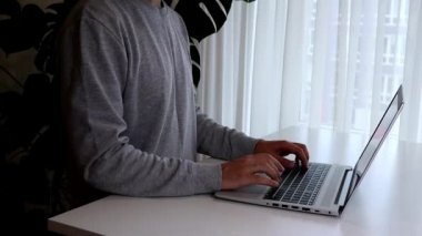 Ev görüşünden çalış. Genç adam dizüstü bilgisayarla çalışıyor. Erkek ayakta ve daktilo ediyor.