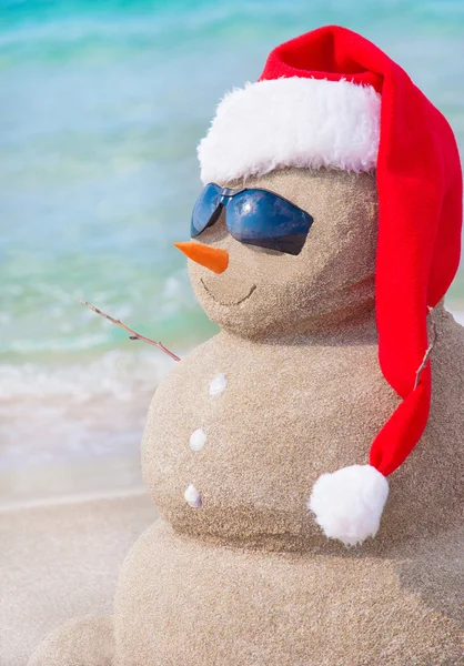 Boneco de neve de Natal em santa chapéu na praia arenosa — Fotografia de Stock