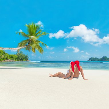 Couple in christmas hats at tropical sandy palm beach clipart