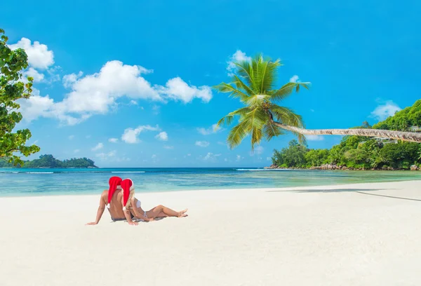 Casal em chapéus de Natal na praia tropical de palmeiras — Fotografia de Stock