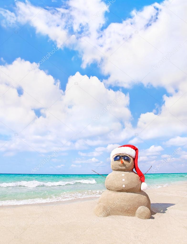 Smiling sandy snowman in red santa hat on the sea beach