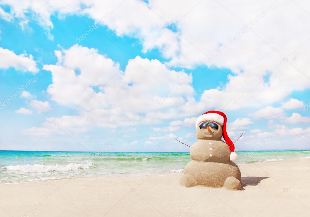 Sandy snowman in santa hat on sea beach
