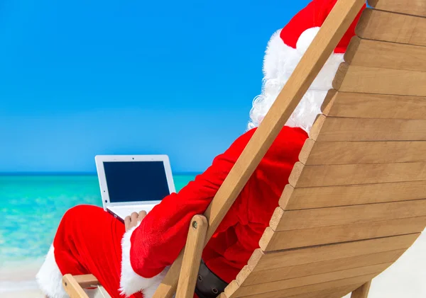 Święty Mikołaj na plaży przy użyciu laptopa — Zdjęcie stockowe