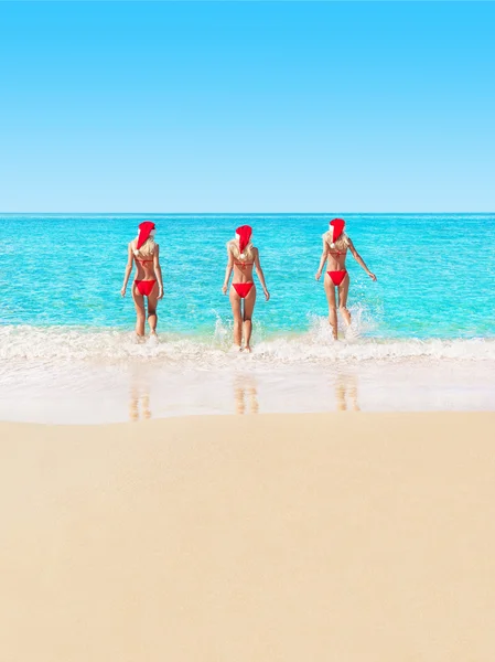 Donne in rosso cappelli di Natale sulla spiaggia — Foto Stock
